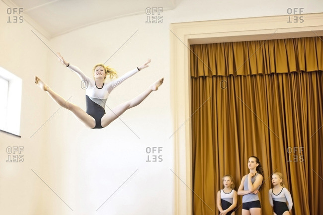 Girl in gymnastics outfit doing aerial jump with three girls watching
