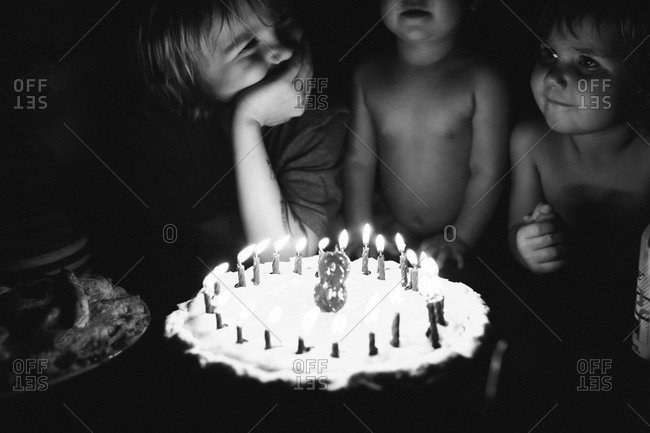 Three kids standing over a birthday cake