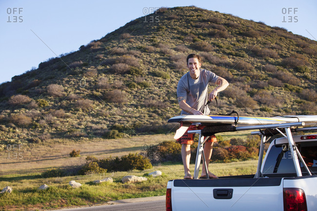 Man standing on back of truck with surfboard