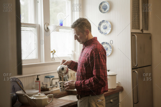 Man pouring himself a cup of coffee from a French press by the kitchen sink