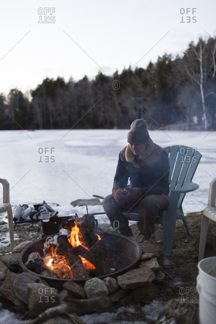 A woman sitting by a fire next to a frozen lake