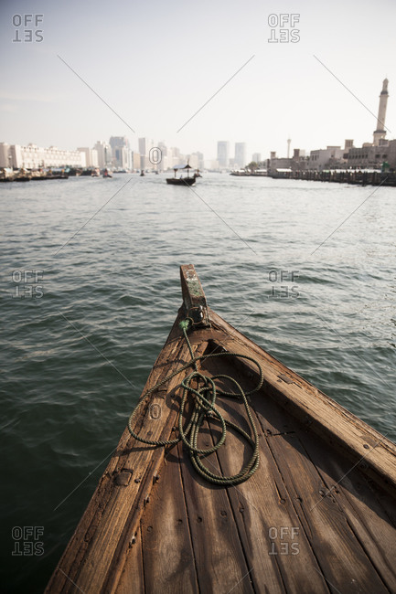 Front of wooden boat on water near city buildings