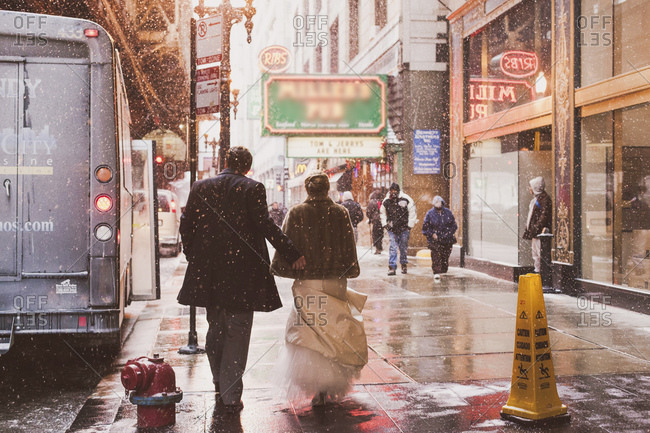 Back view of couple walking during snow fall in downtown Chicago