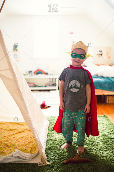 Boy in superhero mask and cape next to indoor tent