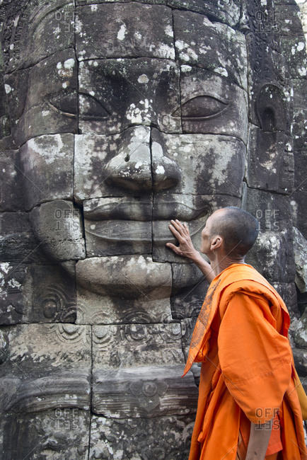 Monk gazing up at carved face in Angkor, Cambodia
