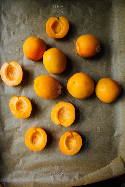 Sliced orange apricots on parchment lined baking sheet with black background