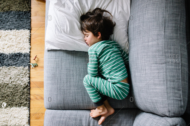 Boy in pajamas curled on couch from above