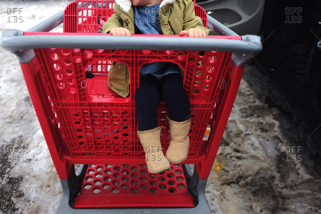 Child riding in shopping cart in snowy parking lot