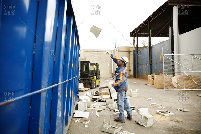A worker tosses computer parts into a bin at a recycling plant