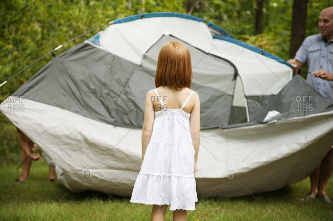 A girl watches her family set up a tent