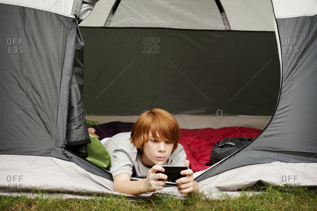 A boy on a smartphone hanging out of a tent