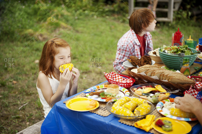 A young girl eats corn at a family picnic