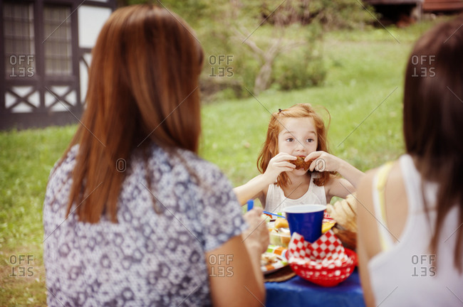 A little girl eats corn on the cob at a family picnic