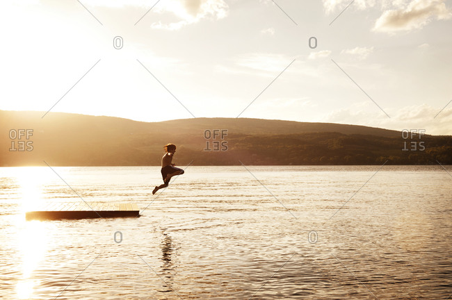 A boy jumps off a floating dock on a lake