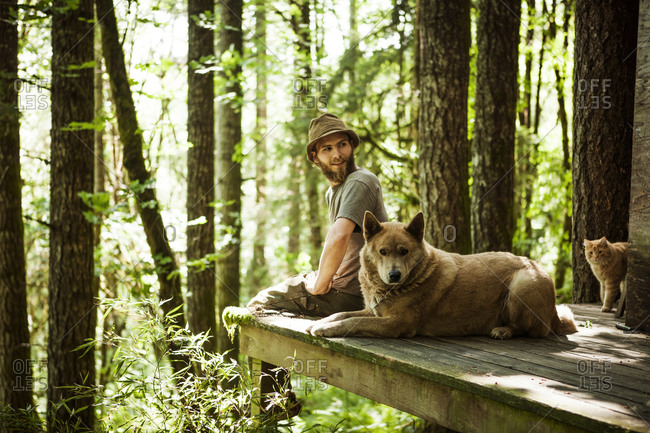Man sitting in a forest with a dog and with a cat