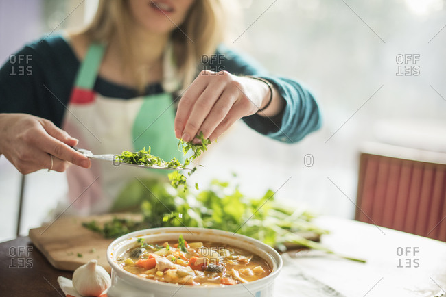 Woman garnishing vegetable stew with fresh herbs