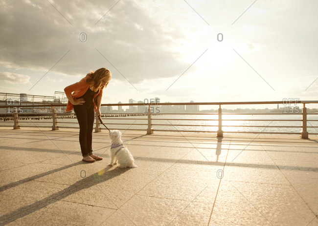 A woman talks to her dog on a pier