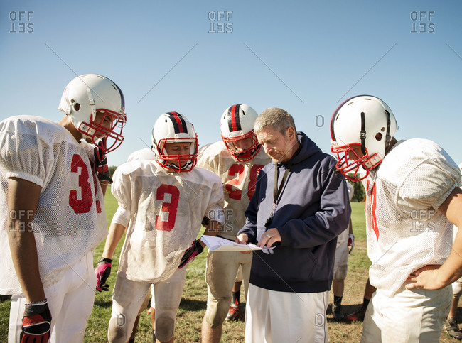 A high school football coach looks over plays with his team