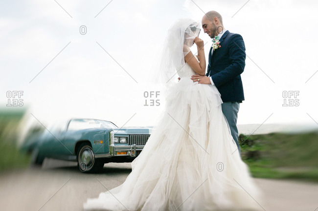 Bride and groom flirting on the road near a vintage car
