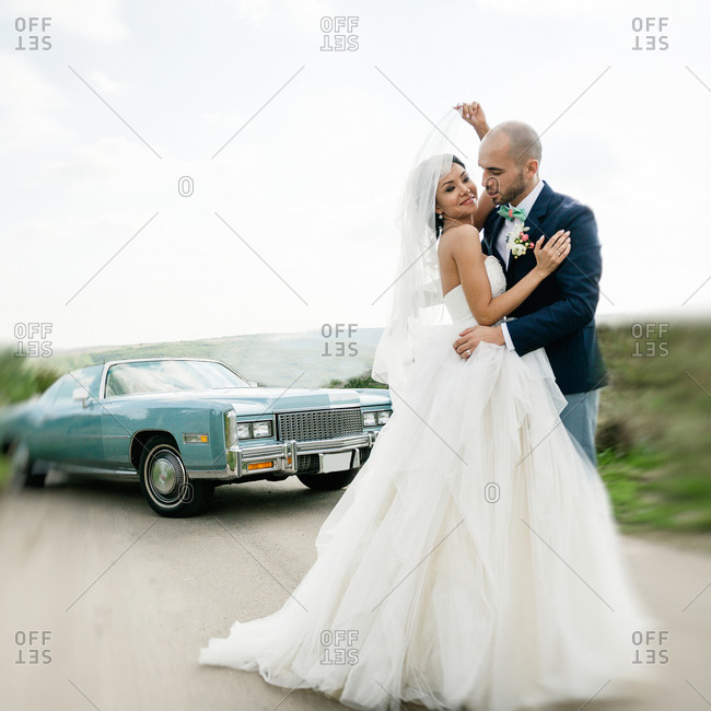 Bride and groom embracing on the road near a vintage car