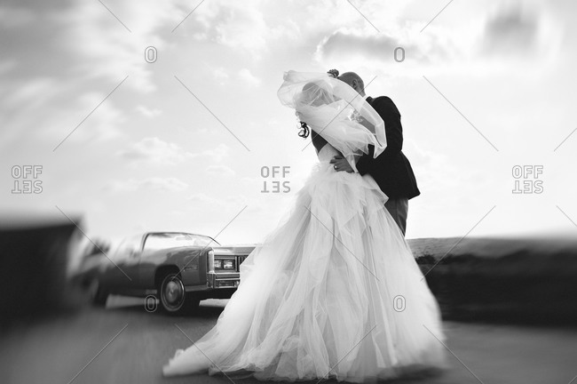 Bride and groom kissing on the road near a vintage car