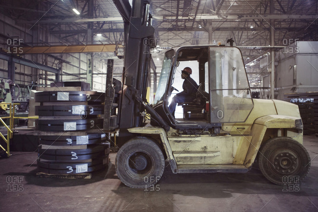 Steel factory worker moving load with forklift