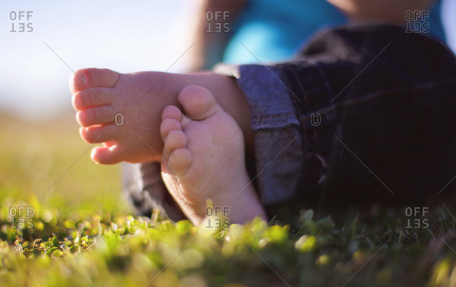 Little crossed feet of a baby sitting in the grass
