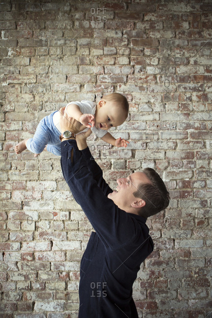 Father lifting up his son by a brick wall