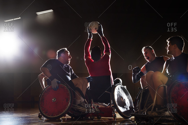 A wheelchair rugby player holds the ball out of reach of other players