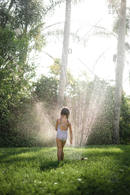 Girl running through sprinkler in her yard
