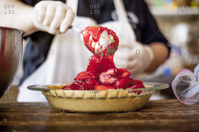 Person spooning strawberry filling into pie shell