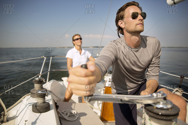 Man at winch of yacht adjusting sails with friend