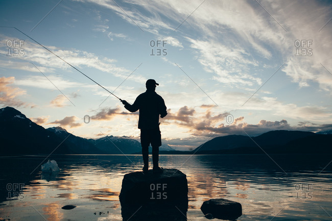 Silhouette of man fly-fishing at dusk in Wachusett Inlet, Glacier Bay National Park