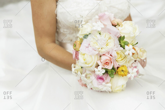 A bride holds a bouquet of pale pink, yellow and white flowers