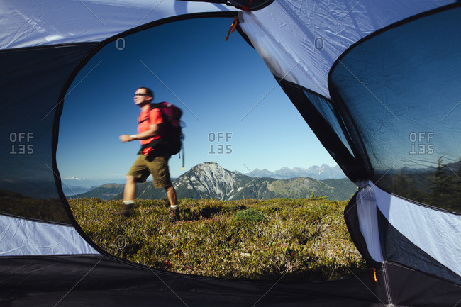 View from inside a camping tent of man hiking across national forest land with Mount Baker in the distance