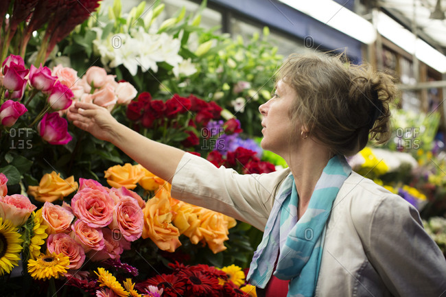 A woman reaches for a pink rose at a floral stand
