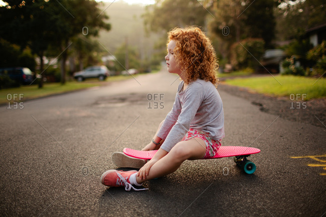 Daydreaming girl sitting on a skateboard in the street