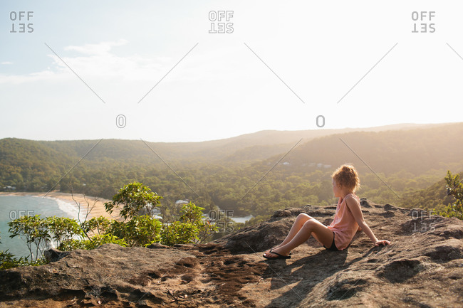 Child seated on rocks taking in the view of beach below