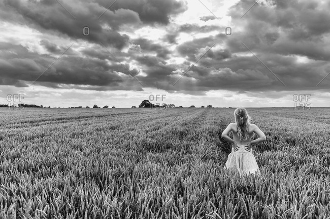 Young woman standing in grain field under dramatic sky