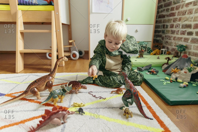 Boy wearing dinosaur costume playing with toy dinosaurs