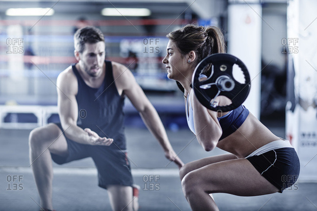 Trainer watching woman doing fitness training with weights