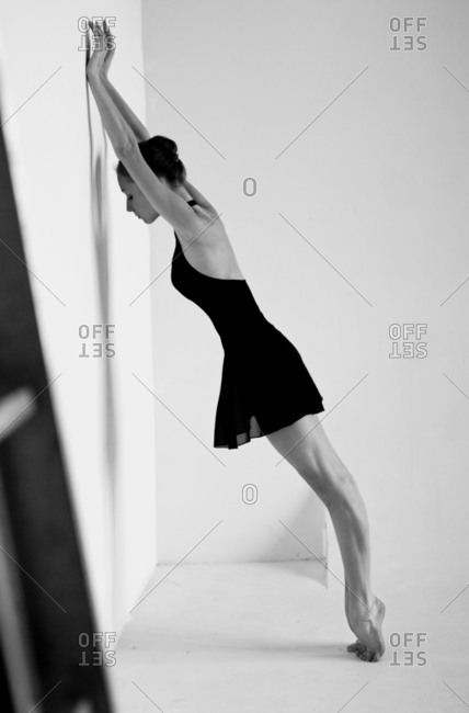 Female dancer in black costume leans against a white wall