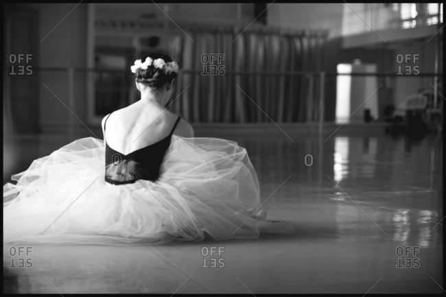 Back of a costumed ballerina seated on the floor of dance studio