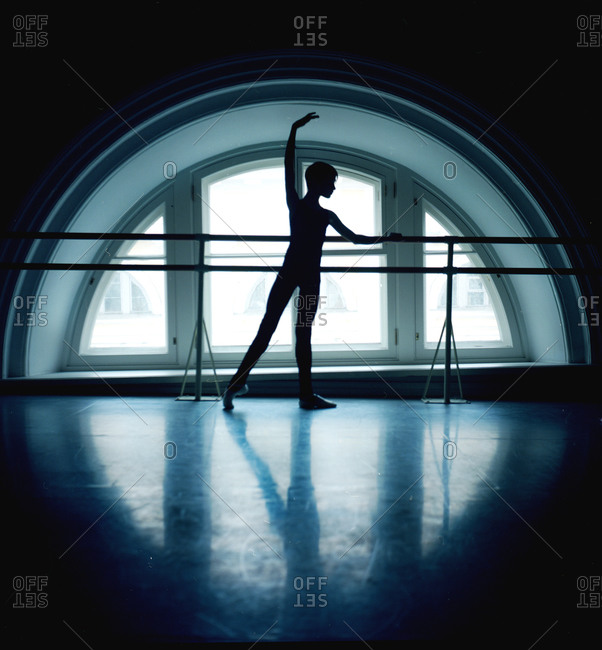 Male dancer silhouetted at barre in front of arched window