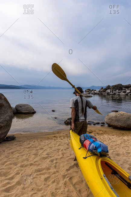 Man with a paddle over his shoulder dragging a kayak
