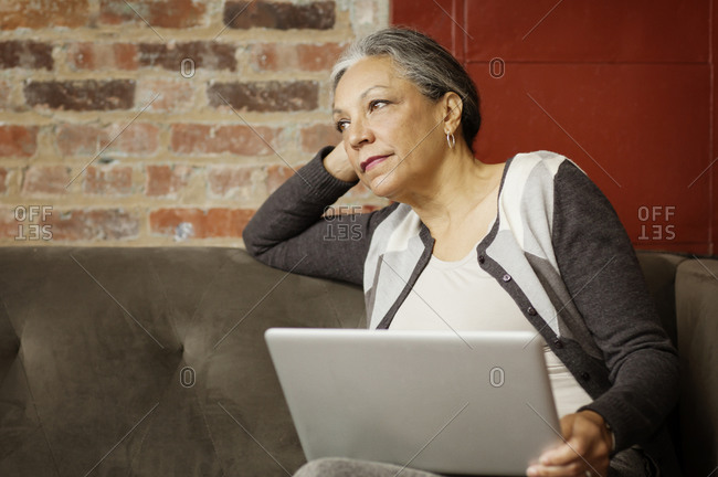 Woman thinking on couch with laptop