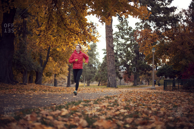 Woman jogging along park path in fall
