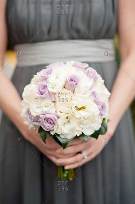 Bridesmaid in gray dress holding bouquet of pale purple and white flowers