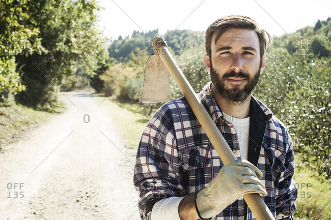 Portrait of rugged man carrying hoe in orchard