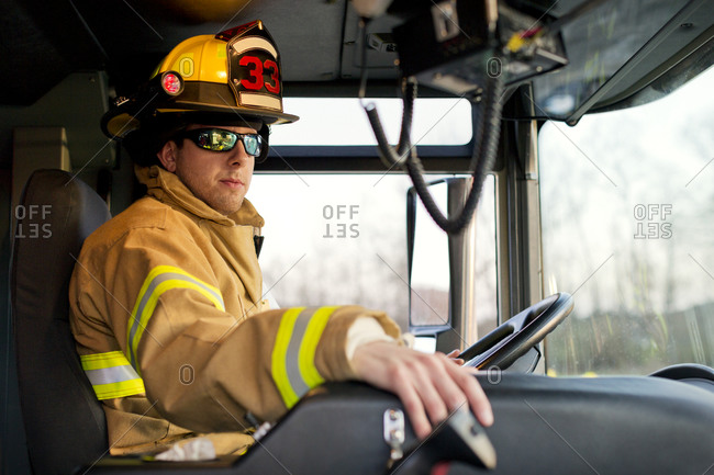 A fireman in the driver\'s seat of a fire engine
